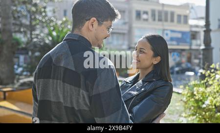 Una coppia amorevole abbraccia una strada della città illuminata dal sole, mostrando un momento di affetto tra un uomo e una donna sullo sfondo urbano. Foto Stock