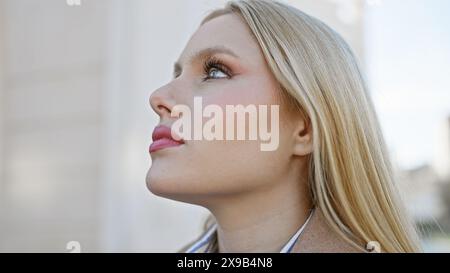 Una giovane donna bionda contemplativa guarda verso l'alto su una strada urbana. Foto Stock