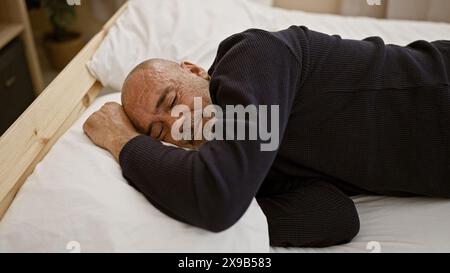 Un uomo barbuto di mezza età con i capelli grigi che dorme tranquillamente in una camera da letto, trasmettendo un tema di riposo e relax. Foto Stock