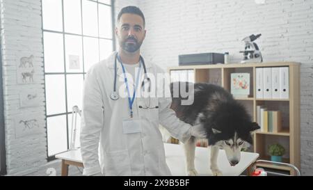 Bel veterinario ispanico in clinica che esamina un husky al chiuso. Foto Stock