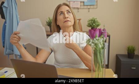 Una donna matura ama se stessa con la carta, che sembra scomoda a causa del calore mentre lavora in ufficio a casa Foto Stock