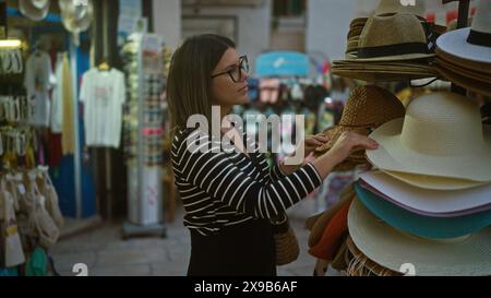 Una giovane donna ispanica che acquista cappelli nelle affascinanti strade di polignano a mare, puglia, italia, durante un piacevole pomeriggio. Foto Stock