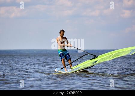 Windsurfer vuole alzare la vela di una tavola a vela e continuare a fare surf in una giornata di sole Foto Stock