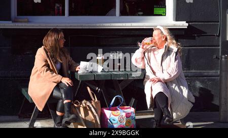 Cardiff, Galles, ottobre 29 2023: Due giovani donne attraenti sedute fuori su una panchina che trascorrono del tempo insieme con un drink. Foto Stock