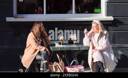 Cardiff, Galles, ottobre 29 2023: Due giovani donne attraenti sedute fuori su una panchina che trascorrono del tempo insieme con un drink. Foto Stock