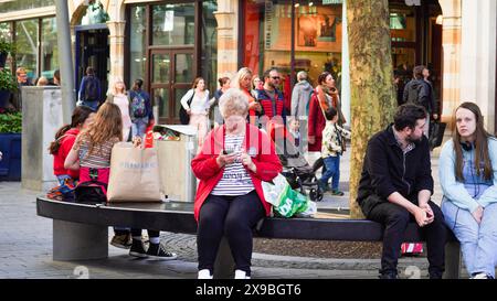 Cardiff, Galles, ottobre 29 2023: Fotografia di strada, pomeriggio intenso nel centro di Cardiff. La gente si siede sulle panchine e una donna anziana controlla il suo telefono Foto Stock