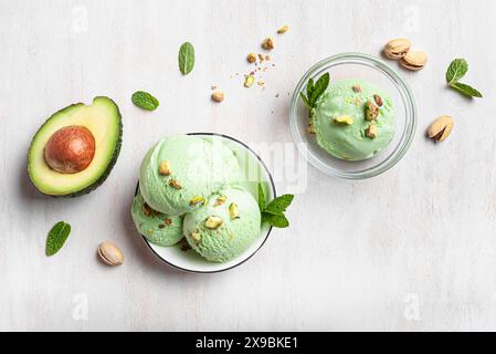 Il gelato verde all'avocado al pistacchio al cocco viene erogato in una ciotola su sfondo bianco in legno. Gelato vegano alla moda fatto in casa con avocado verde. Foto Stock