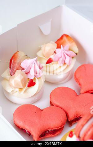 Set di dolci per San Valentino o per qualsiasi giorno romantico confezionati in una scatola di cartone. Macaron a forma di cuore e mini torte Foto Stock