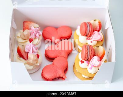 Set di dolci per San Valentino o per qualsiasi giorno romantico confezionati in una scatola di cartone. Macaron a forma di cuore e mini torte Foto Stock