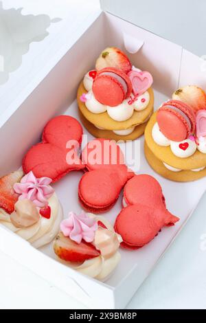 Set di dolci per San Valentino o per qualsiasi giorno romantico confezionati in una scatola di cartone. Macaron a forma di cuore e mini torte Foto Stock