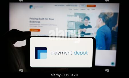 Persona che detiene un cellulare con il logo della società di elaborazione carte USA Payment Depot (Stax Payments) di fronte alla pagina Web. Mettere a fuoco il display del telefono. Foto Stock