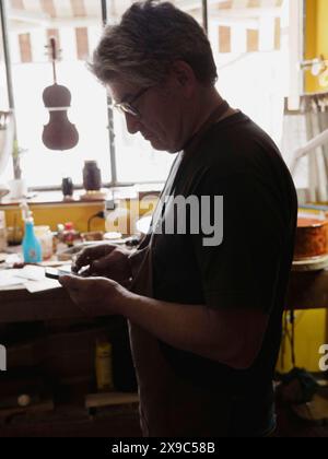 Artigiano si è concentrato sul lavoro in un'officina illuminata dal sole con vari strumenti e strumenti Foto Stock