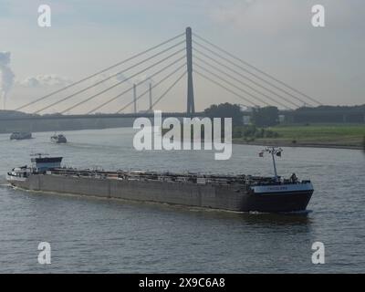 Nave da carico che navigava il fiume sotto un ponte di primo piano, industria sullo sfondo, traffico marittimo sul Reno vicino a Wesel in una mattinata nebbiosa Foto Stock