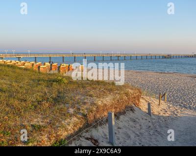 Molo che conduce al mare calmo, dune ricoperte di erba in primo piano al tramonto, atmosfera autunnale sulla spiaggia di Binz con alberi sdraio Foto Stock