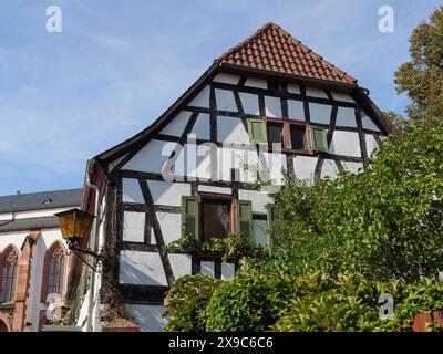 Una casa in legno con persiane verdi e piante da giardino accanto a una chiesa gotica sotto un cielo soleggiato, storiche case in legno nel Foto Stock