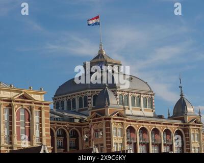 Edificio storico con bandiera olandese di fronte a un cielo blu, la spiaggia di scheveningen con molo e il lungomare, scheveningen, paesi bassi Foto Stock