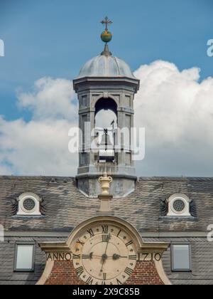 Una torre dell'orologio con campane e un grande orologio su un edificio storico del castello sotto un cielo nuvoloso, un vecchio castello di mattoni rossi con torri e un grande parco con Foto Stock