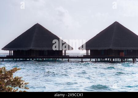 Due tradizionali bungalow sull'acqua con tetti di paglia situati su palafitte sopra le acque turchesi delle Maldive. La scena cattura la tranquillità Foto Stock