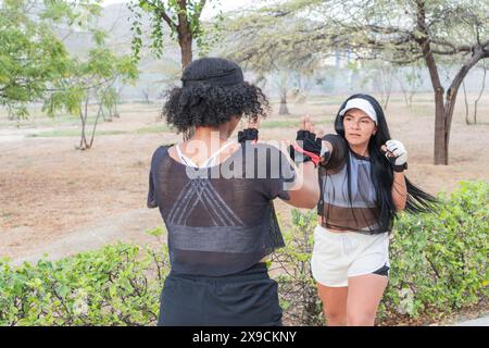 Due donne che praticano tecniche di autodifesa in un parco all'aperto, dimostrando mosse di blocco e colpi durante la loro sessione di allenamento. Foto Stock