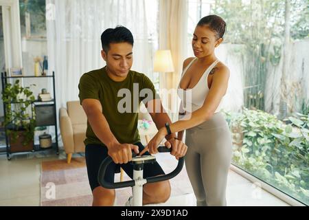 Un uomo e una donna che lavorano insieme per regolare le impostazioni su una cyclette in un moderno soggiorno Foto Stock