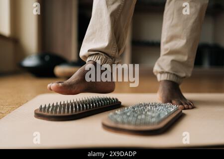 Primo piano di piedi neri maschili irriconoscibili che salgono sulla tavola sadhu godendosi una pratica consapevole nella soleggiata sala di meditazione. Concetto di medicina alternativa Foto Stock