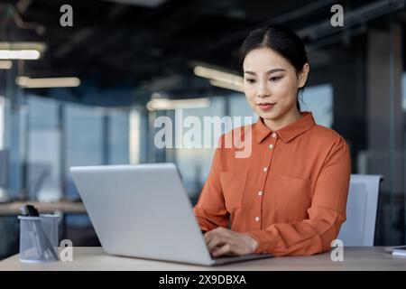Donna asiatica seria che lavora in ufficio con un laptop, donna d'affari che scrive sulla tastiera, donna d'affari che prepara un rapporto elettronico, rapporto sui risultati finanziari dell'azienda. Foto Stock
