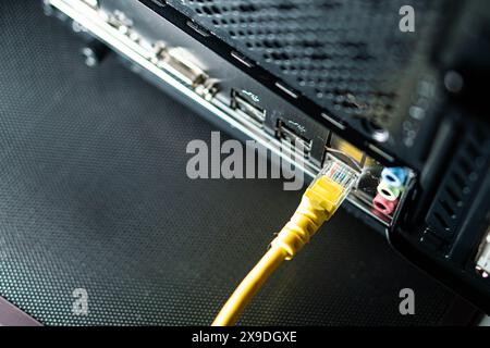 Primo piano di un cavo Ethernet giallo collegato al retro di un computer. L'immagine mostra la porta di rete e le altre porte periferiche del computer. Foto Stock