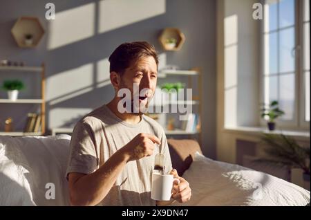L'uomo assonnato si sveglia preparando il tè in una tazza e sbadigliando la mattina. Foto Stock