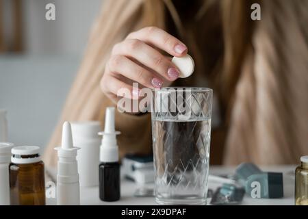 La grande donna caucasica è avvolta in una coperta, trema, si sente male e ha una temperatura elevata. primo piano di una mano che lancia un effervescente Foto Stock