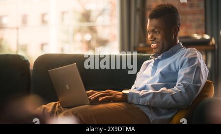 Concentrated Black male Working from Home, utilizza un computer portatile. Influenza la digitazione della personalità su Internet sulla tastiera e la navigazione in Internet. Concetto personale freelance e Millennial Professional. Foto Stock