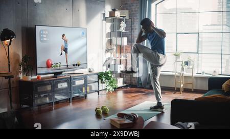 Vista laterale: Strong Black Sportsman fa esercizi di allenamento a casa, utilizza corsi di esercizi online, Personal Video Trainer in streaming fitness Tutorial. Forte atleta afroamericano maschile. Foto Stock