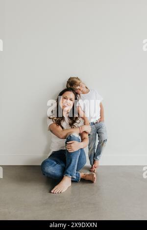 La mamma siede sul pavimento contro il muro mentre la figlia sta in piedi e appoggia la testa Foto Stock