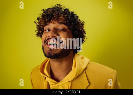 Il bell'indiano con i capelli ricci si posa con sicurezza in una felpa con cappuccio giallo brillante. Foto Stock