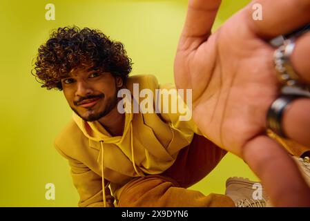 Bell'uomo indiano con capelli ricci che posa in una felpa gialla con cappuccio su uno sfondo vivido. Foto Stock