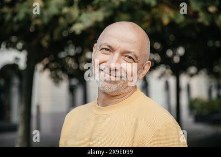 Senior Man in maglione giallo sorride dolcemente in un ambiente urbano Foto Stock