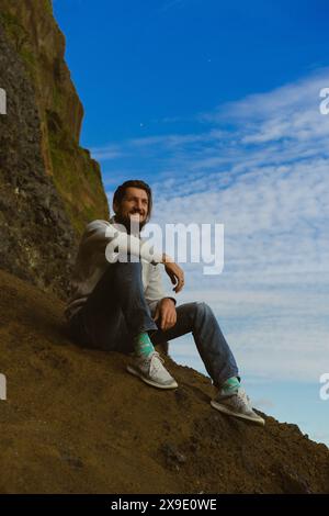 Uomo seduto sulle colonne della Reynisfjara sulla spiaggia di Reynisdrangar. Foto Stock