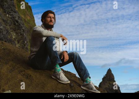 Uomo seduto sulle colonne della Reynisfjara sulla spiaggia di Reynisdrangar. Foto Stock