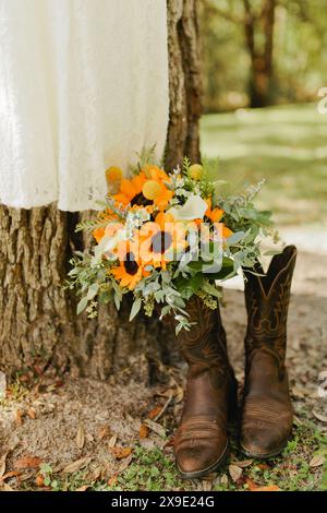 Il bouquet nuziale di girasole si trova in stivali da cowgirl con abito Foto Stock