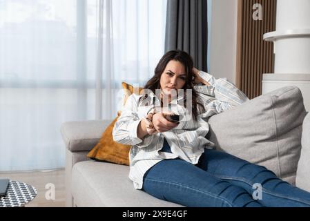 Concetto di pigrizia. Giovane donna pigra sdraiata sul divano a guardare la televisione nel suo tempo libero. Attività del fine settimana di donna d'affari quando non ha niente Foto Stock