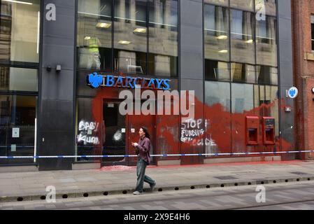 Barclays Bank, Mosley Street, centro di Manchester, Regno Unito, una porta di vetro si è rotta e coperta di vernice rossa il 31 maggio 2024. La polizia ha messo in atto un cordone. Negli ultimi mesi i manifestanti pro-Palestina hanno preso di mira questa banca e gettato vernice rossa ad altre imprese che credono stiano sostenendo Israele. I graffiti sul fronte includono: "Smettete di finanziare il genocidio”. Foto Stock