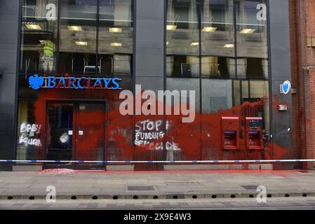 Barclays Bank, Mosley Street, centro di Manchester, Regno Unito, una porta di vetro si è rotta e coperta di vernice rossa il 31 maggio 2024. La polizia ha messo in atto un cordone. Negli ultimi mesi i manifestanti pro-Palestina hanno preso di mira questa banca e gettato vernice rossa ad altre imprese che credono stiano sostenendo Israele. I graffiti sul fronte includono: "Smettete di finanziare il genocidio”. Foto Stock