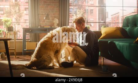 Felice bello giovane Gioca con il suo cane a casa, splendido Golden Retriever. Attraente uomo seduto su un pavimento che stuzzica, accarezza e gratta un cane eccitato, divertiti nell'elegante appartamento. Foto Stock