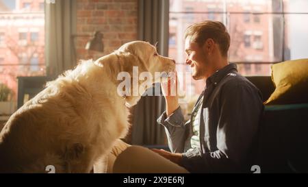 Felice bello giovane Gioca con il suo cane a casa, splendido Golden Retriever. Attraente uomo seduto su un pavimento che stuzzica, accarezza e gratta un cane eccitato, divertiti nell'appartamento moderno. Foto Stock