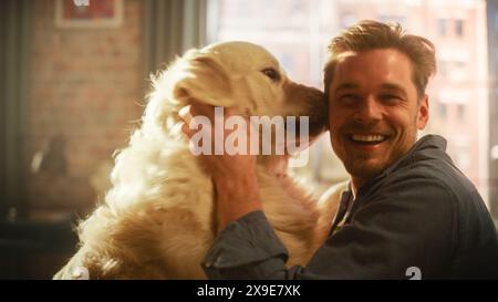 Felice bello giovane Gioca con il suo cane a casa, splendido Golden Retriever. Uomo attraente seduto su un pavimento. Eccitato cane leccare il proprietario che prende in giro il cucciolo. Divertiti nell'elegante appartamento. Foto Stock