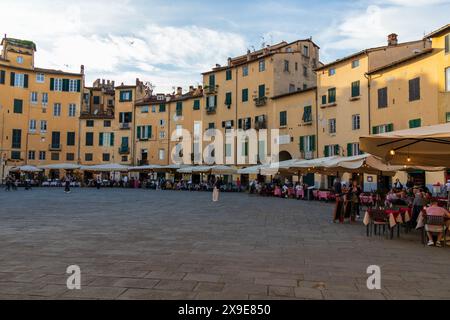 Turisti ed edifici sulla splendida Piazza dell'Anfiteatro nella storica città medievale di Lucca in Toscana in una serata di sole vicino al tramonto. Foto Stock