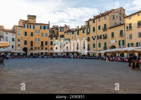 Turisti ed edifici sulla splendida Piazza dell'Anfiteatro nella storica città medievale di Lucca in Toscana in una serata di sole vicino al tramonto. Foto Stock