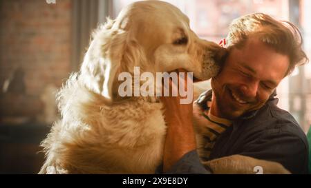 Felice bello giovane Gioca con Dog at Home, splendido Golden Retriever. Uomo attraente seduto su un pavimento. Eccitato cane leccare il proprietario che prende in giro il cucciolo. Divertimento nell'elegante appartamento. Foto Stock