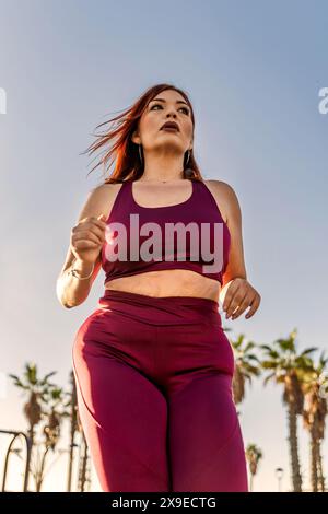 Donna di categoria superiore che corre all'aperto con abbigliamento sportivo marrone, dimostrando determinazione e motivazione fisica, stile di vita sano, giorno luminoso e soleggiato, AC Foto Stock