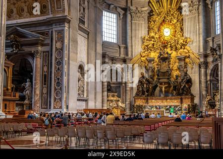 Le persone che partecipano a una messa Basilica di San Pietro di fronte alla Cattedra di San Pietro racchiusa in un involucro scolpito in bronzo dorato disegnato da Bernini. Foto Stock
