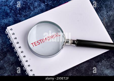 TESTIMONIANZA scritta attraverso una lente d'ingrandimento in un taccuino su uno sfondo blu eterogeneo Foto Stock